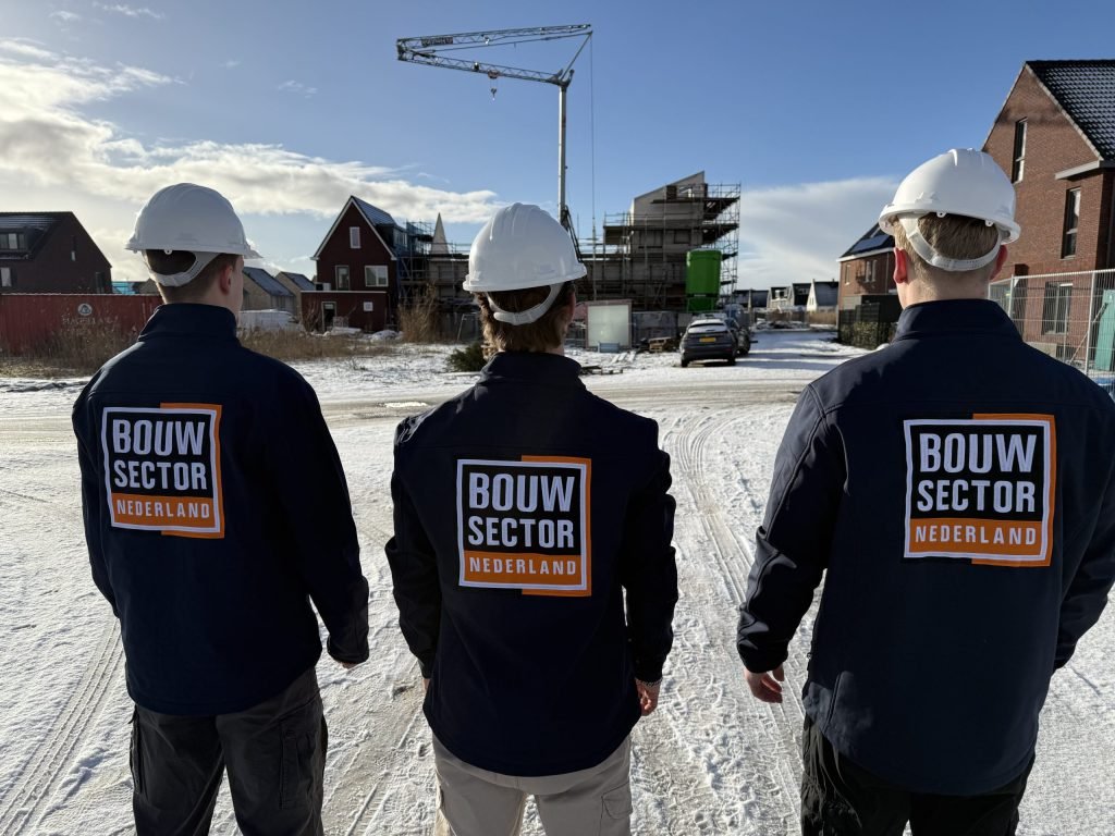 Drie vakmensen in werkjassen met logo kijken naar rijen woningen op een winterdag